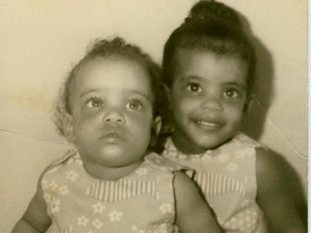 Angela as a toddler with her baby sister, in matching dresses